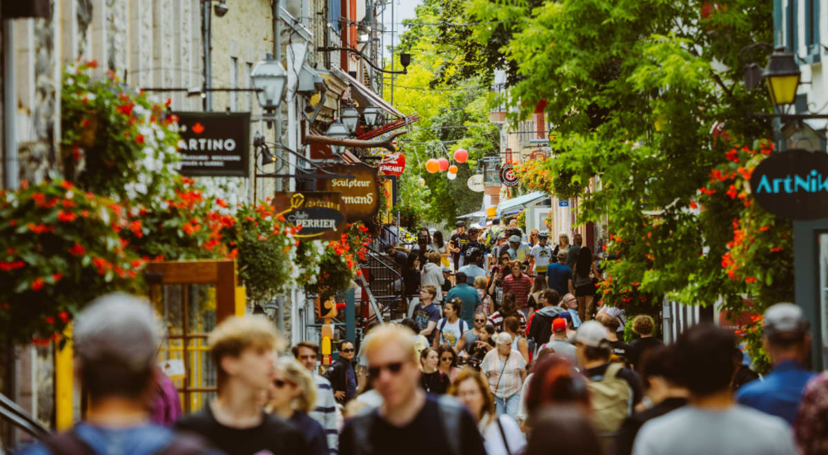 Une scène de rue animée et colorée, avec une foule de gens qui déambulent parmi les boutiques, les restaurants et une végétation luxuriante en arrière-plan.