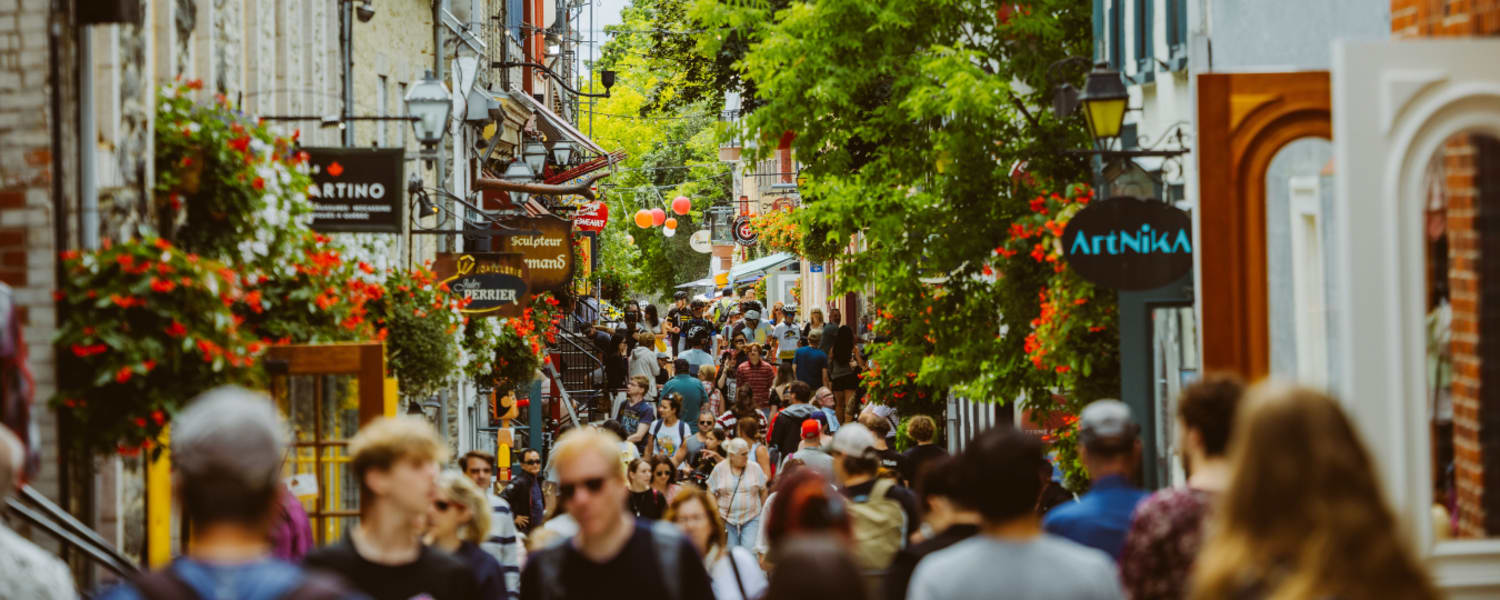 Une scène de rue animée et colorée, avec une foule de gens qui déambulent parmi les boutiques, les restaurants et une végétation luxuriante en arrière-plan.