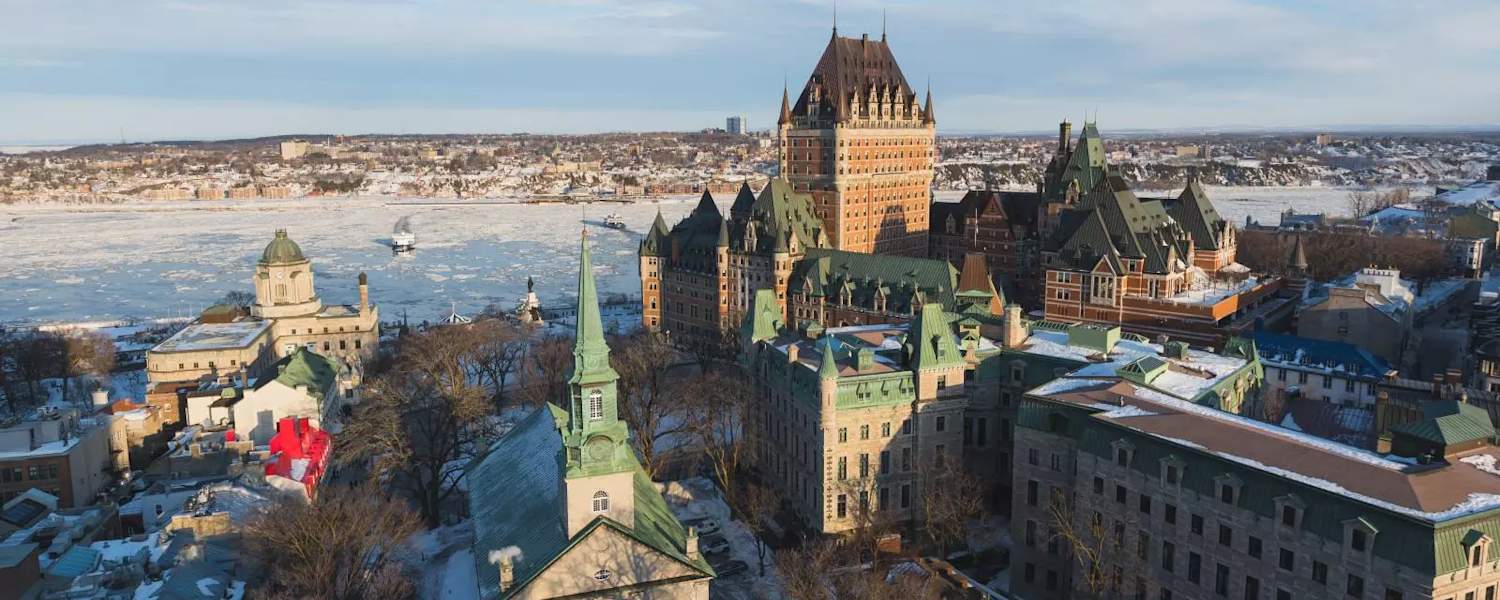 Vue panoramique d'un paysage urbain enneigé, mêlant styles architecturaux historiques et modernes, avec ses hautes flèches et ses dômes, sur fond de ciel bleu azur.