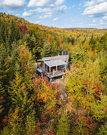 Un chalet rustique niché au cœur d'une forêt aux couleurs automnales éclatantes, offrant une vue panoramique imprenable sur les collines et les vallées environnantes.