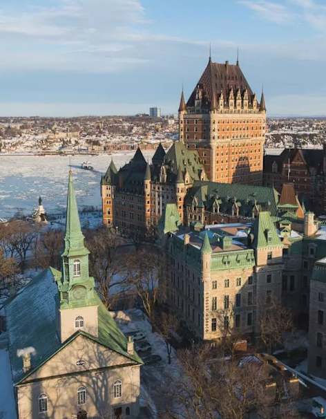 Vue panoramique d'un paysage urbain enneigé, mêlant styles architecturaux historiques et modernes, avec ses hautes flèches et ses dômes, sur fond de ciel bleu azur.