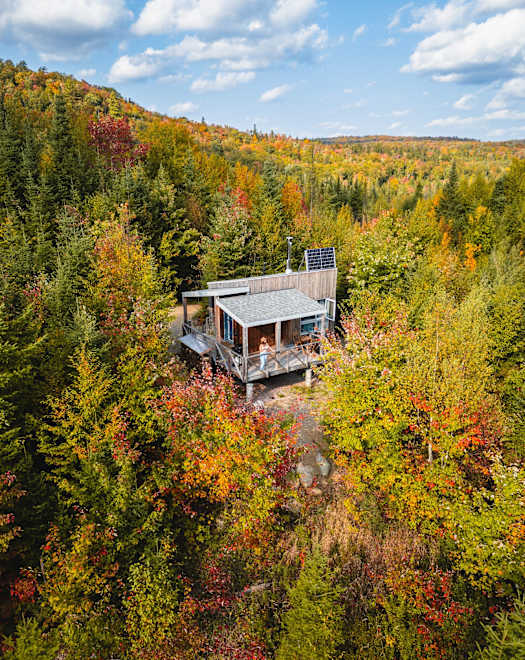 Un chalet rustique niché au cœur d'une forêt aux couleurs automnales éclatantes, offrant une vue panoramique imprenable sur les collines et les vallées environnantes.