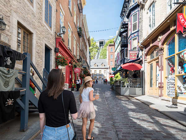 Deux femmes marchent dans une ruelle pavée du Petit-Champlain en été, bordée de bâtiments en pierre et de commerces