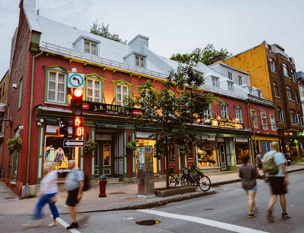 Une scène de rue animée et colorée, mêlant architecture traditionnelle et moderne, grouillante de piétons et de cyclistes au premier plan.