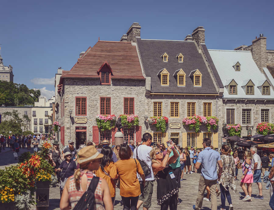 Foule de visiteurs et touristes marchent sur la Place-Royale en été, devant des maisons historiques en pierre colorées avec mansardes
