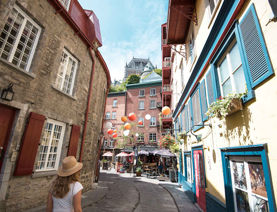 Une femme marche dans la rue Petit-Champlain en été, bordée de maisons colorées historiques et décorées de ballons